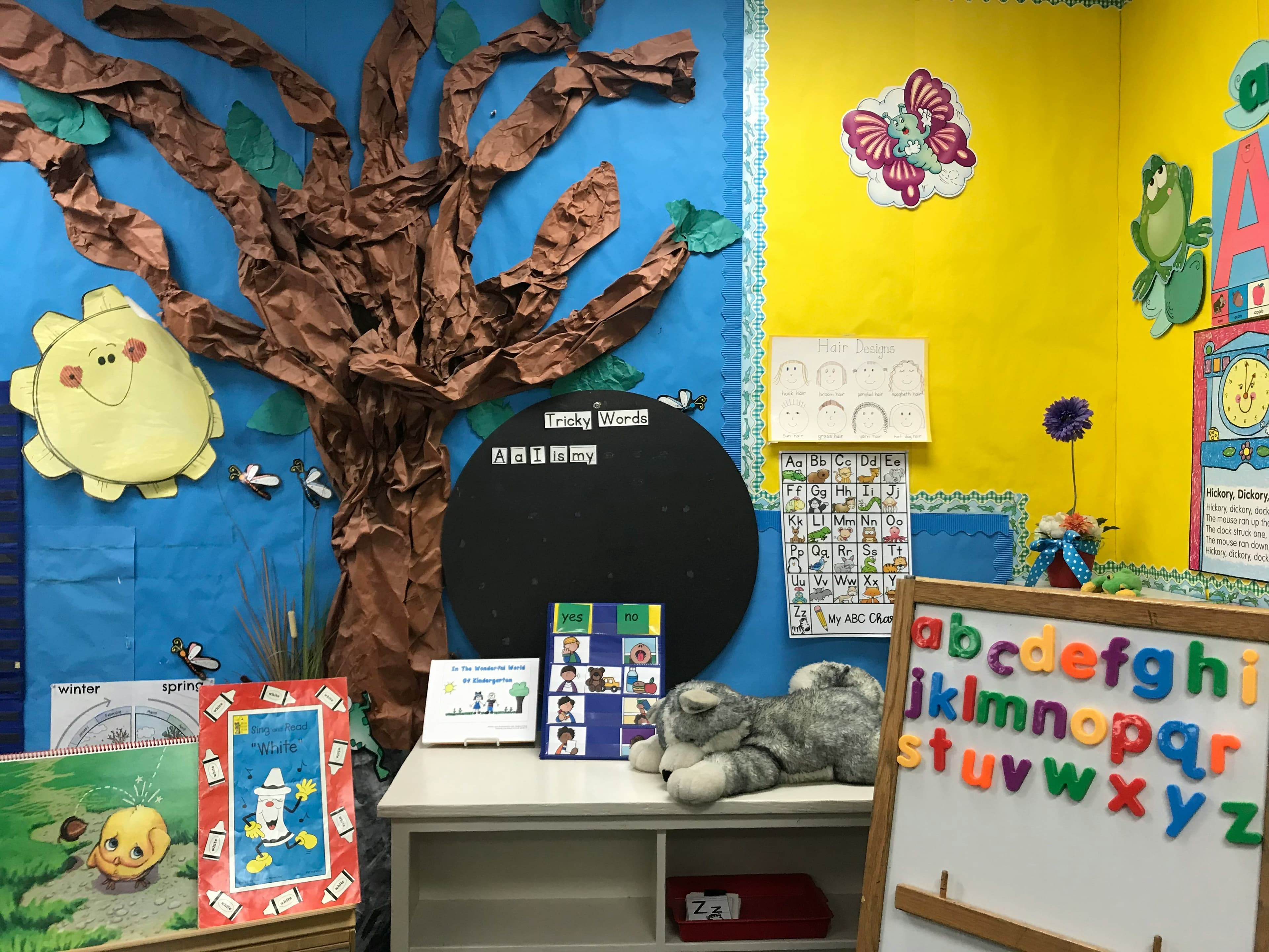 A kindergarten classroom with alphabet posters, magnetic letters, and a paper-tree wall.